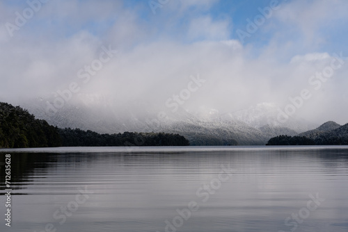 andscape with snow-capped mountains shrouded by clouds and reflected in the lake