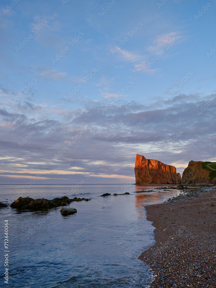 The beautiful colors, natural arch and shape of famous Perce Rock on the Gaspe Peninsula in Quebec Canada at sunset with it's red-pinkish colors from the shores of Perce Village The beautiful colors, natural arch and shape of famous Perce Rock on the Gaspe Peninsula in Quebec Canada at sunset with it's red-pinkish colors from the shores of Perce Village