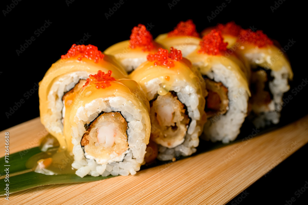 Side view closeup of sushi rolls covered in yellow sauce and topped with red caviar