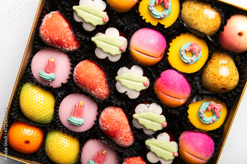 Box of rainbow marzipan sweets in form of different fruits and cakes photo