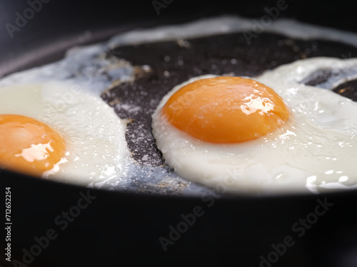 Two fried eggs seasoned with sea salt in a frying pan. Close up.