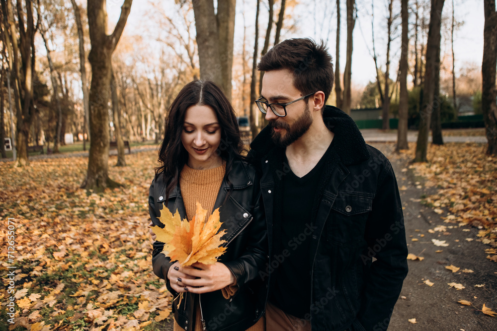 Heterosexual caucasian young loving couple walking outside in the city park in sunny weather, hugging smiling kissing laughing spending time together. Autumn, fall season, orange yellow red maple leav Heterosexual caucasian young loving couple walking outside in the city park in sunny weather, hugging smiling kissing laughing spending time together. Autumn, fall season, orange yellow red maple leav