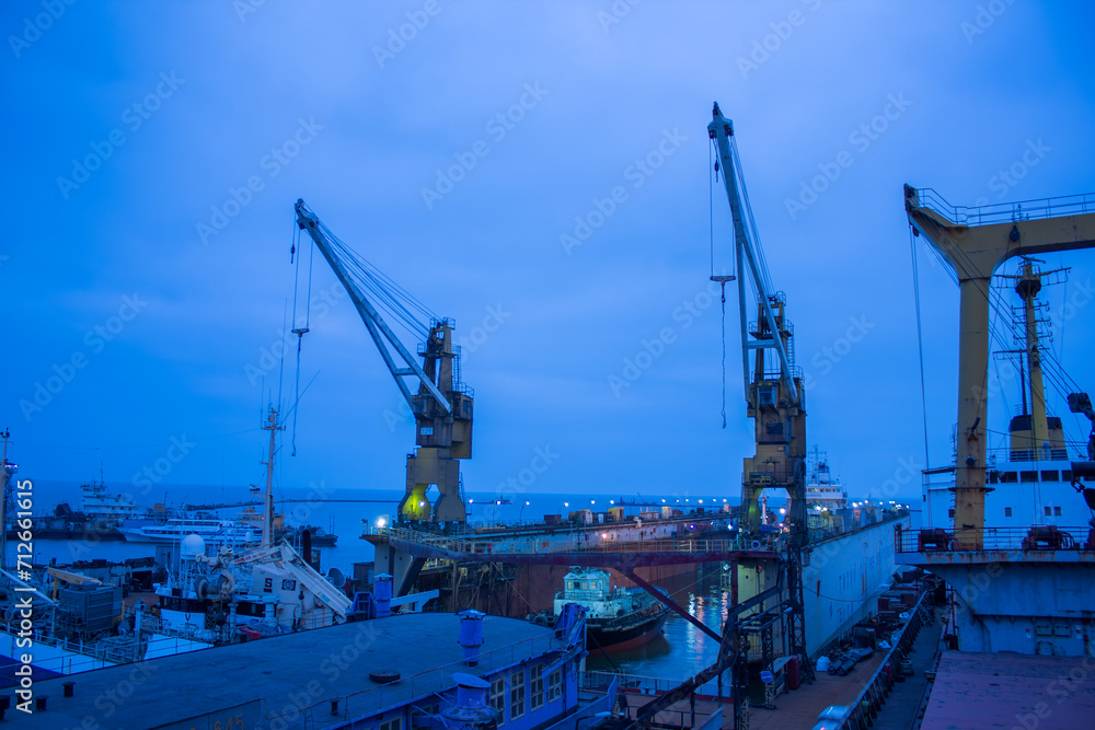 Industrial shipyard at dusk, floating dry dock with ship under repair, cranes standby. Maritime vessel maintenance, night sky, heavy machinery, shipbuilding, naval engineering scene. Industrial shipyard at dusk, floating dry dock with ship under repair, cranes standby. Maritime vessel maintenance, night sky, heavy machinery, shipbuilding, naval engineering scene.