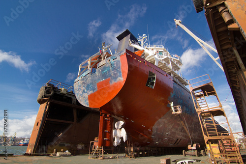 Commercial vessel in dry dock for maintenance. Ship undergoes hull painting and repairs. Maritime, industrial shipping process. Workers refurbish boat. Dockyard activity, sea transport upgrade.