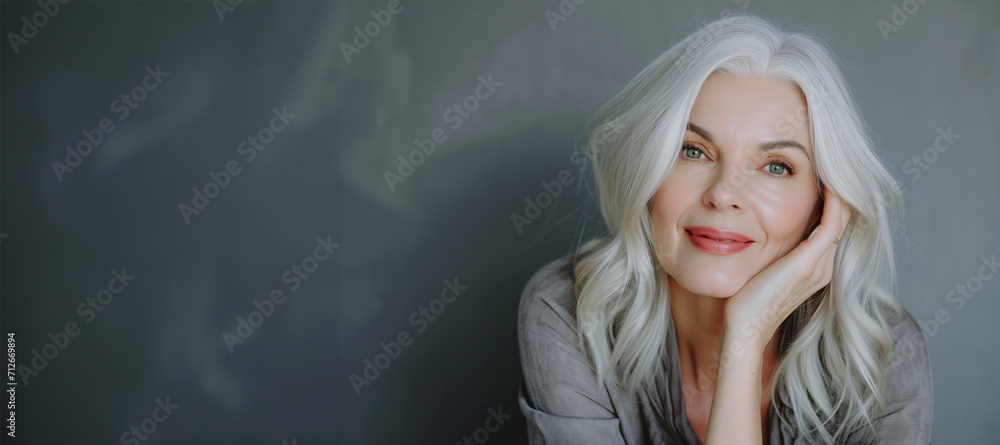 Close-up portrait of half face of cheerful middle-aged Asian 50s woman with silver gray long hair, attractive lady looks at camera and laughing. Mature model with naked shoulders isolated on brown Close-up portrait of half face of cheerful middle-aged Asian 50s woman with silver gray long hair, attractive lady looks at camera and laughing. Mature model with naked shoulders isolated on brown
