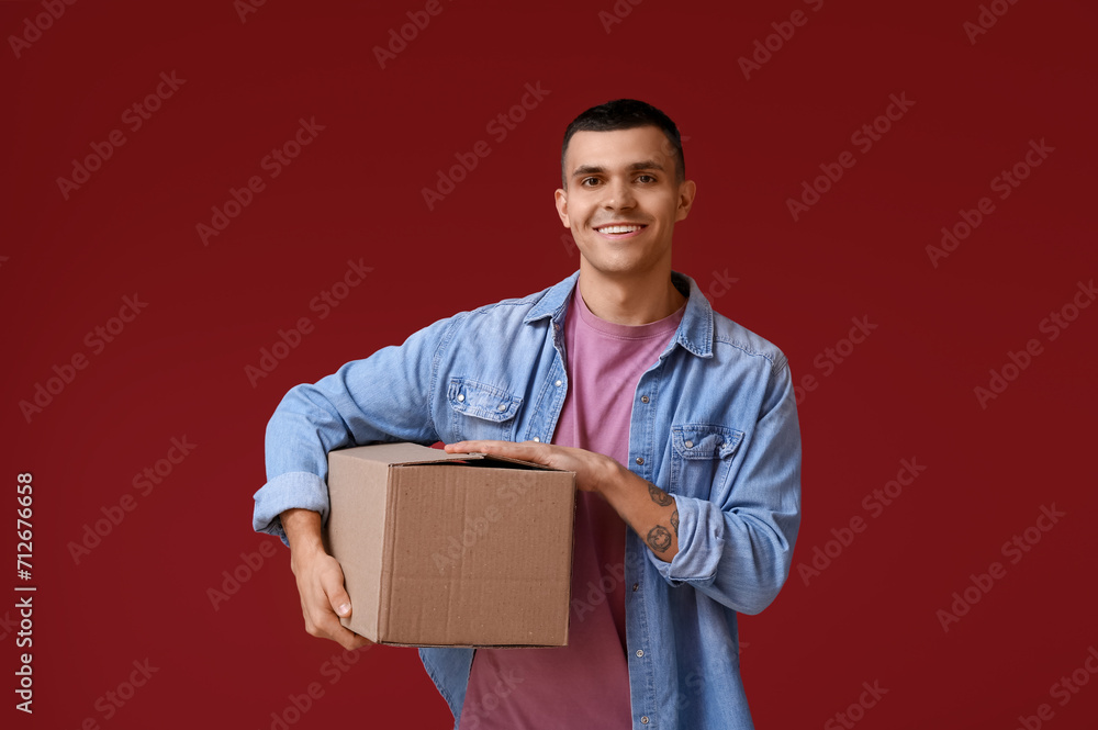 Handsome young man holding parcel on red background Handsome young man holding parcel on red background
