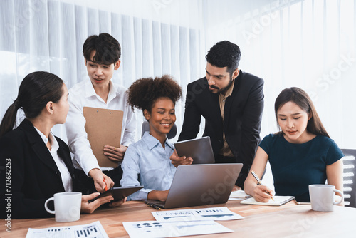 Multiracial analyst team use BI dashboard data to analyze financial report on meeting table. Group of diverse business people utilize data analysis by FIntech for success business marketing. Concord