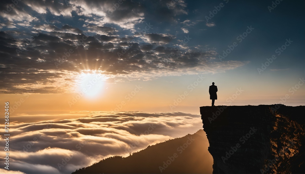 Man on cliff's edge witnessing the sunrise and clouds over the horizon