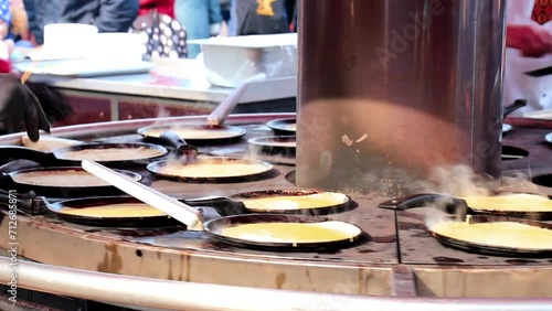 Street food. The cook cooks, fries, bakes pancakes in street cafe on frying pan, professional pancake machine at street fair, fast food. Chef preparing food photo