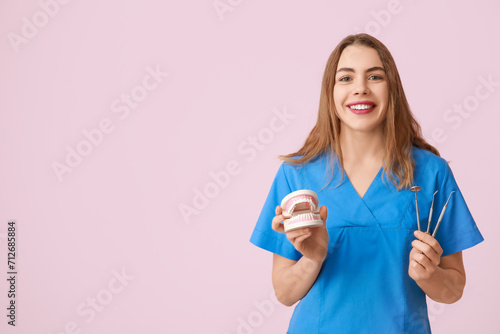 Female dentist with dental tools and jaw model on pink background. World Dentist Day
