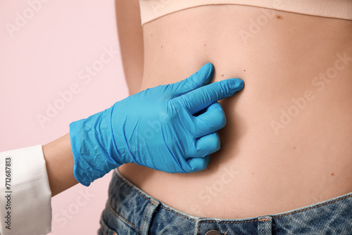 Dermatologist examining young woman with moles on pink background, closeup photo