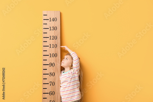 Cute little girl measuring height on yellow background photo