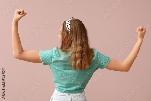 Happy young pin-up woman showing her muscles on pink background, back view photo