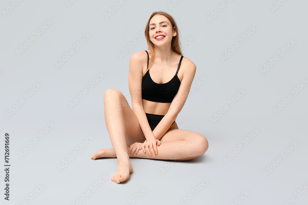Beautiful young woman in black cotton underwear sitting against light background