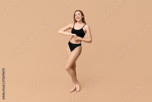Pretty young woman in black cotton underwear on beige background