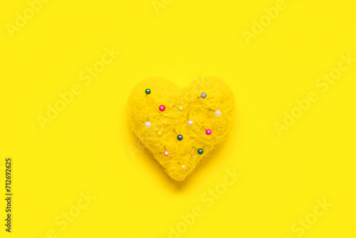 Heart-shaped pincushion with needles on yellow background. Valentine's day celebration photo