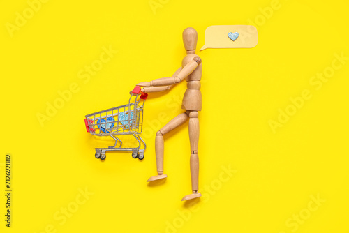 Creative composition with wooden mannequin and shopping cart on yellow background. Valentine's day celebration