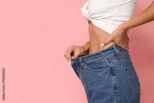 Young woman in loose jeans after weight loss on pink background, closeup