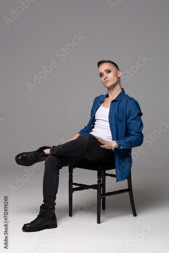 A young man in a blue shirt with the makeup of a rock musician sits on a chair.