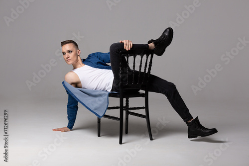 A young man in a blue shirt with rock musician makeup poses on a chair.