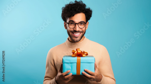 Closeup portrait of a brunet man holding gift box on isolated blue background with space for copy © GulArt