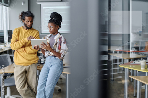 Indian male office worker helping his african american female colleague with code on digital tablet