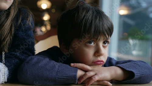 Foto Bored small boy complaining, sulking child feeling annoyed leaning on restaurant