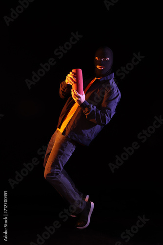 Handsome young man in balaclava with wireless portable speaker on black background