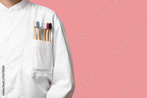 Female dentist with different toothbrushes in her pocket on pink background