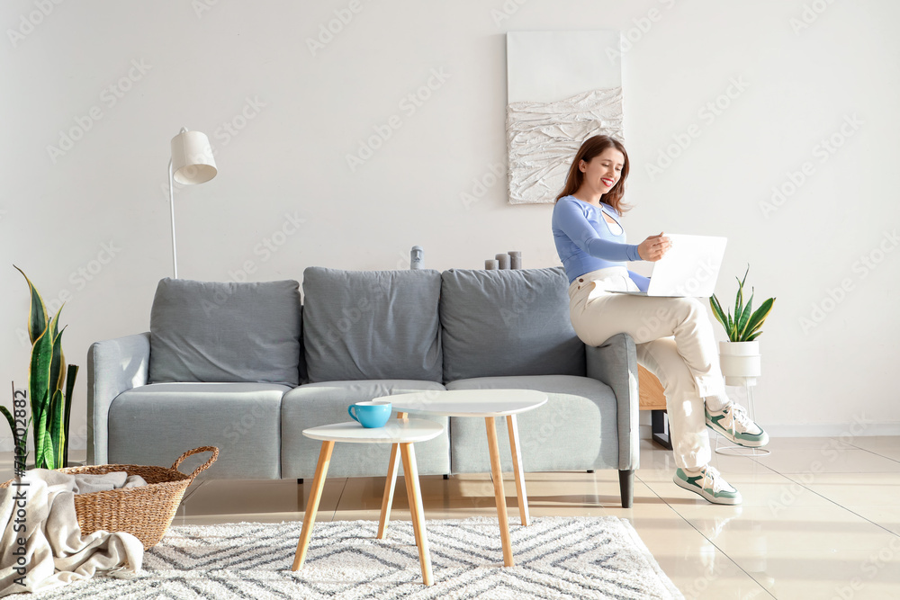 Young woman using laptop on grey sofa at home Young woman using laptop on grey sofa at home