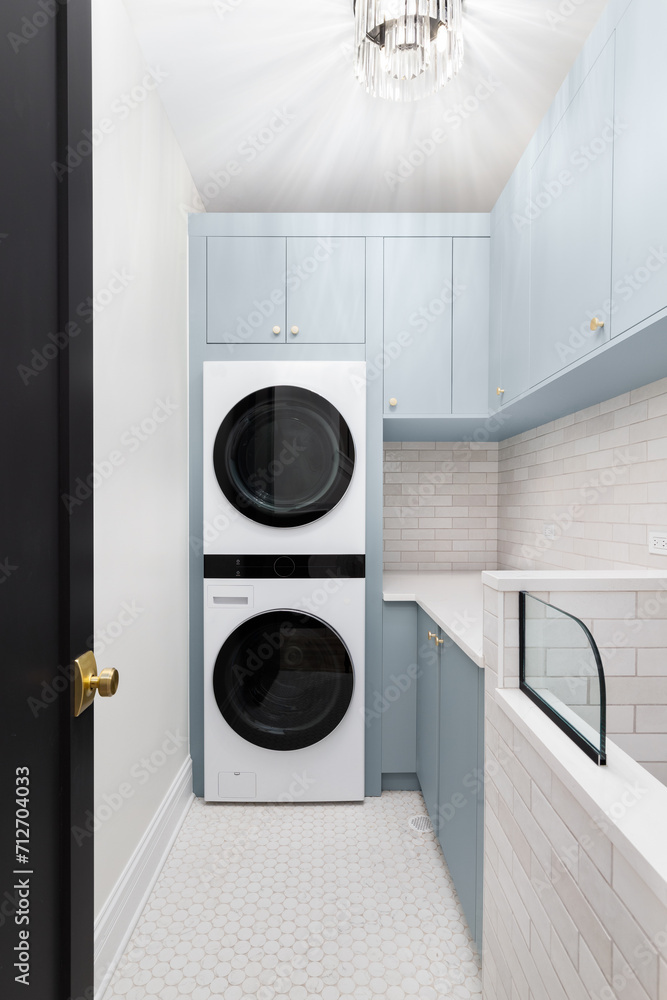 A laundry room with blue cabinets, white washer and dryer, circular tile flooring, subway tile backsplash, and a chandelier hanging above. A laundry room with blue cabinets, white washer and dryer, circular tile flooring, subway tile backsplash, and a chandelier hanging above.
