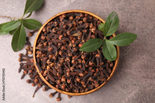 Aromatic cloves and green leaves in bowl on brown table, top view