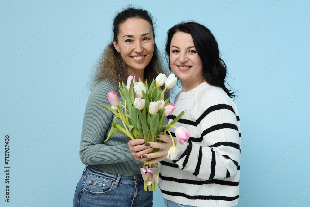Happy mature women with bouquet of beautiful tulips on blue background. International Women's Day Happy mature women with bouquet of beautiful tulips on blue background. International Women's Day