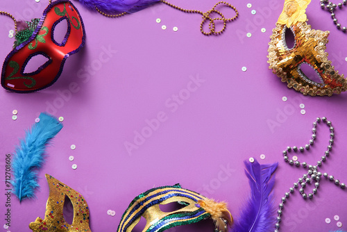 Frame made of carnival masks with feathers and beads for Mardi Gras celebration on purple background