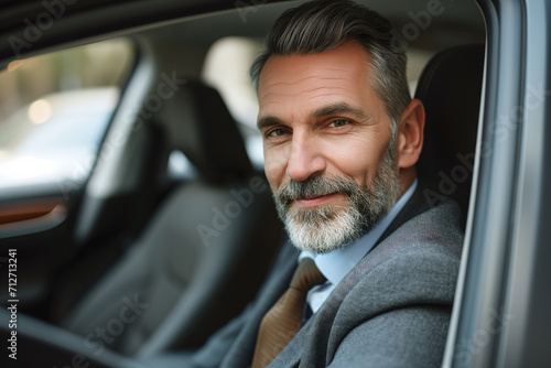 Portrait of handsome 40-year-old man with beard, looking at camera and smiling, sitting in car.
