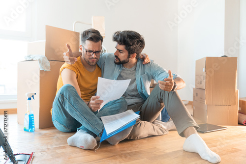 Worried gay couple having financial problems looking at paper documents arguing in new apartment. photo