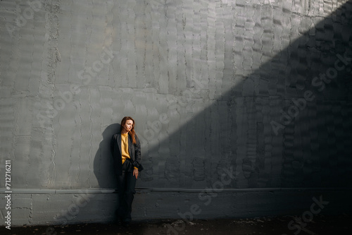 A person standing outdoors in front of a wall, casting a shadow on the ground. 5585