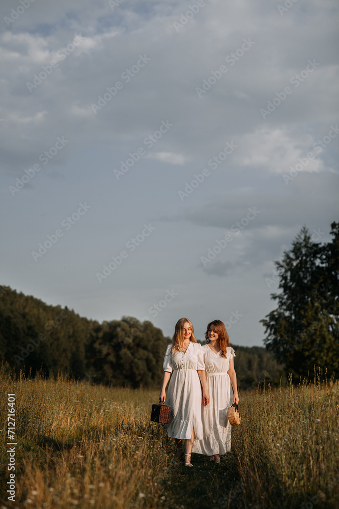 The image features two women in white dresses standing in a field of tall grass. 5621