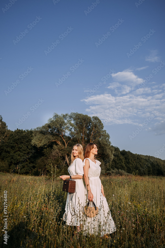 The image shows two women standing in a field with a blue sky and green grass in the background. 5637