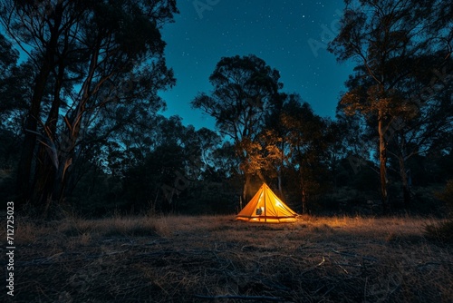 Night and warm light exposure of an illuminated bell tent surrounded by trees and a small camp fire at night  outdoor camping lifestyle
