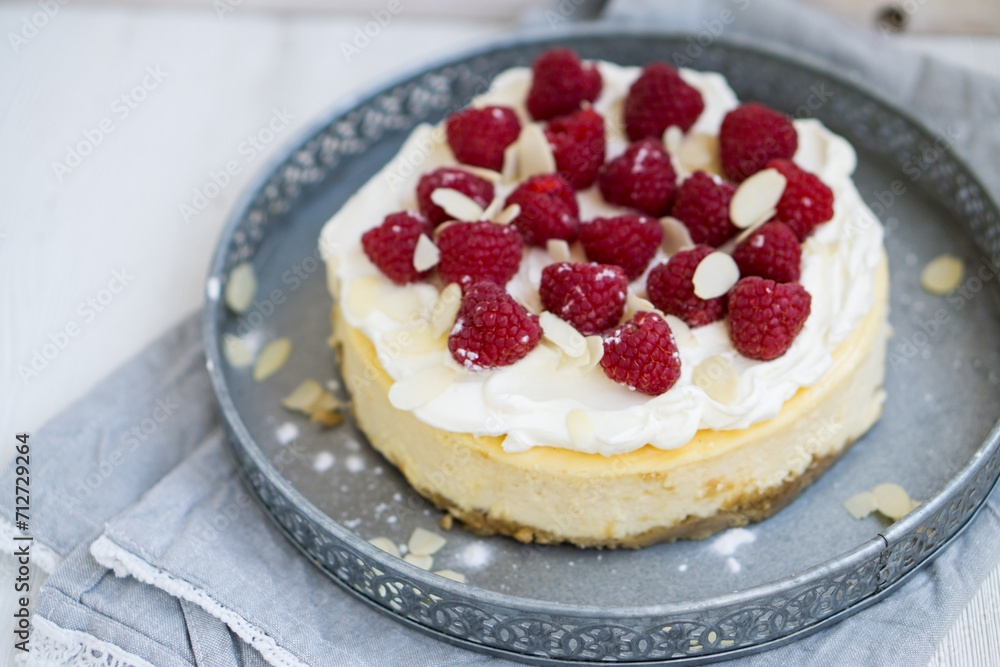 Classic New York cheesecake with whipped cream on top and fresh raspberries on white wooden background close up selective focus Classic New York cheesecake with whipped cream on top and fresh raspberries on white wooden background close up selective focus