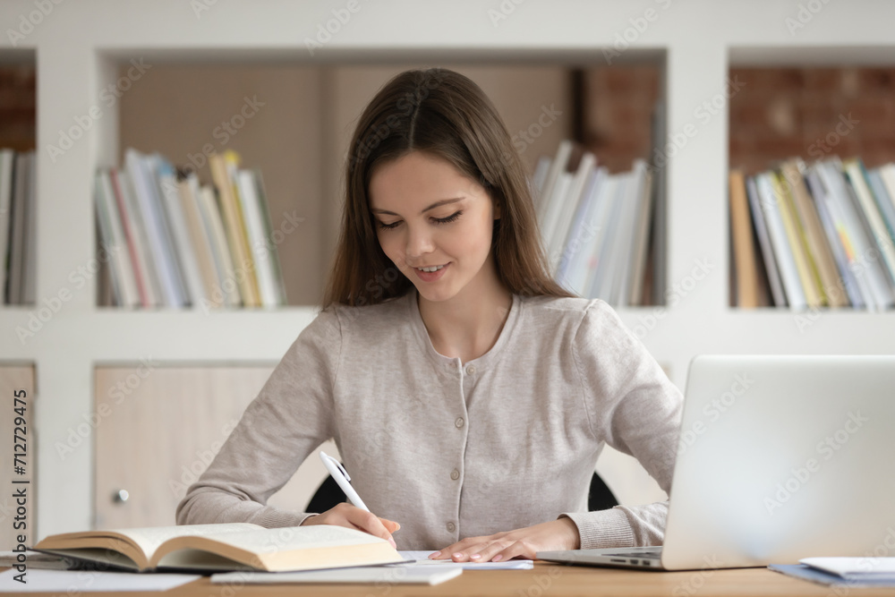 Concentrated female Caucasian student sit at desk studying with laptop write do homework in notebook, focused millennial girl busy preparing for test or exam make notes handwriting, education concept Concentrated female Caucasian student sit at desk studying with laptop write do homework in notebook, focused millennial girl busy preparing for test or exam make notes handwriting, education concept