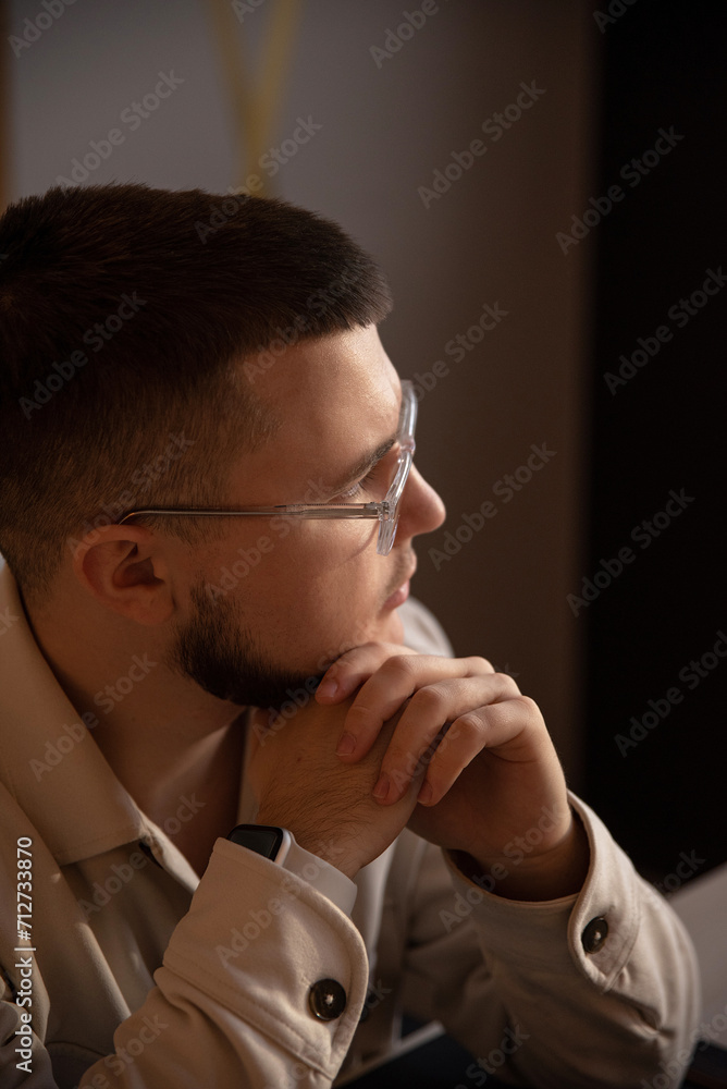 A young guy with glasses holds his chin with his hands A young guy with glasses holds his chin with his hands