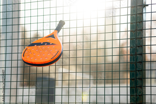 Quadro em tela Photo of a padel racket hooked on the fence of a wall of an outdoor padel court at sunset