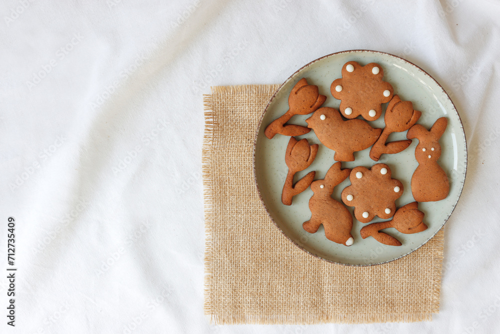 Osterkekse auf Keramikteller, auf einem Jute-Set und weißer Baumwolltischdecke