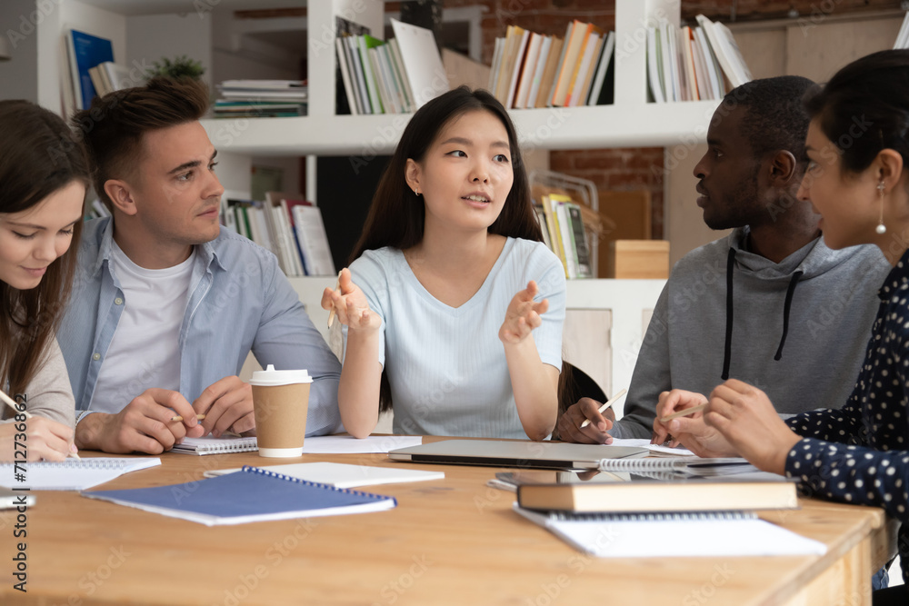 © fizkes - Focused international students sit at desk discuss school educational project brainstorm together, concentrated multiethnic young people study at shared table consider work on paperwork in classroom
