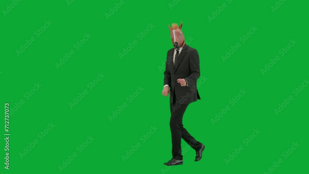 Man in business suit with horse head mask on green studio background. Businessman walking, pointing fingers in the direction and showing thumbs up gesture. Concept of hard office work. Half turn. Man in business suit with horse head mask on green studio background. Businessman walking, pointing fingers in the direction and showing thumbs up gesture. Concept of hard office work. Half turn.