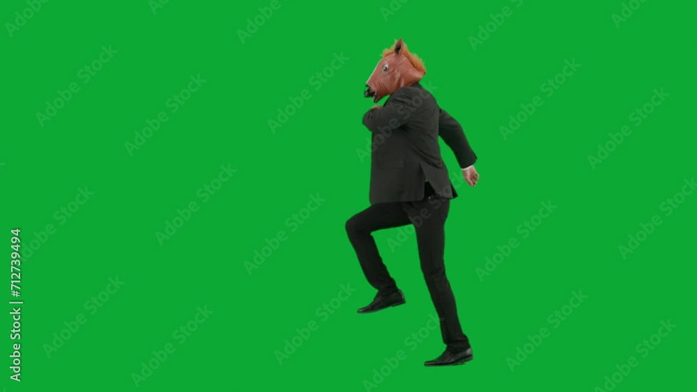 Man in business suit with horse head mask on green studio background. Businessman walking, bouncing and dancing. Concept of hard office work. Side view. Man in business suit with horse head mask on green studio background. Businessman walking, bouncing and dancing. Concept of hard office work. Side view.