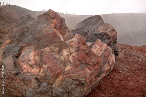 Volcanic rock at the top of Mount Aetna with hikers in the background around the ledge in Silicly, Italy.
 photo