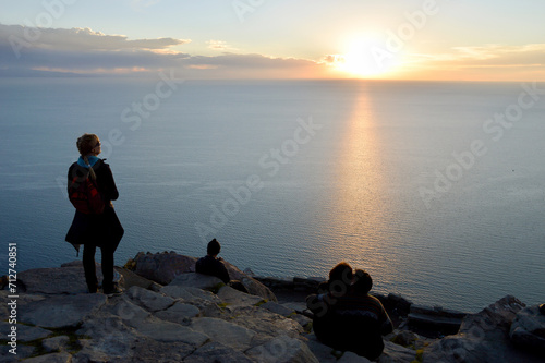 Tourists at a stone viewpoint watching the sunset over Lake Titicaca
